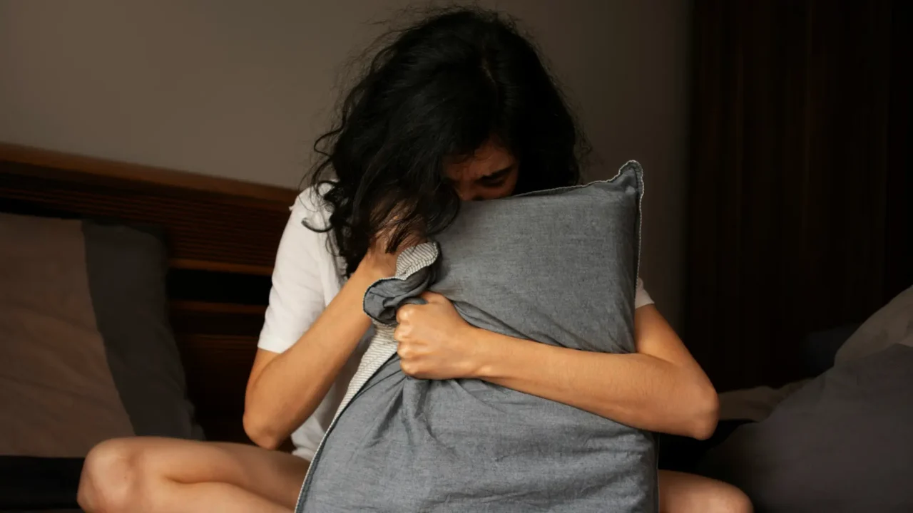 Woman in bed clutching her pillow, looking stressed | High-Functioning Anxiety and Perfectionism | Elnita Ottey & Associates