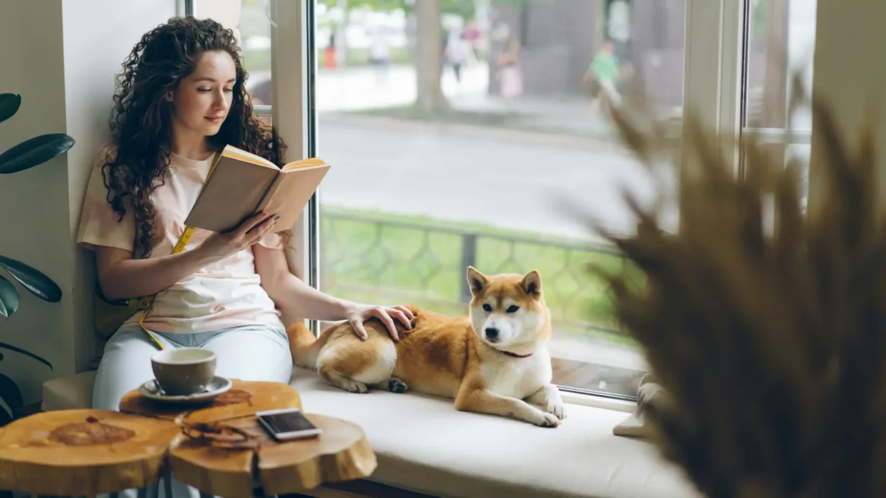 Woman relaxing with her dog in a bay window reading a book | High-Functioning Anxiety and Perfectionism | Elnita Ottey & Associates