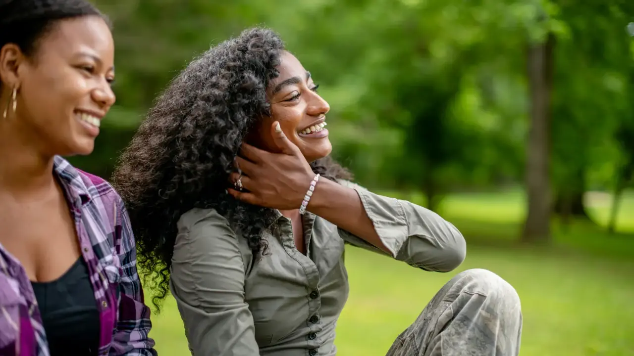 Workplace Trauma and Burnout: Why Rest Alone Isn't Fixing It 2 Woman smiling with friend at the park | Workplace Trauma and Burnout | Elnita Ottey & Associates